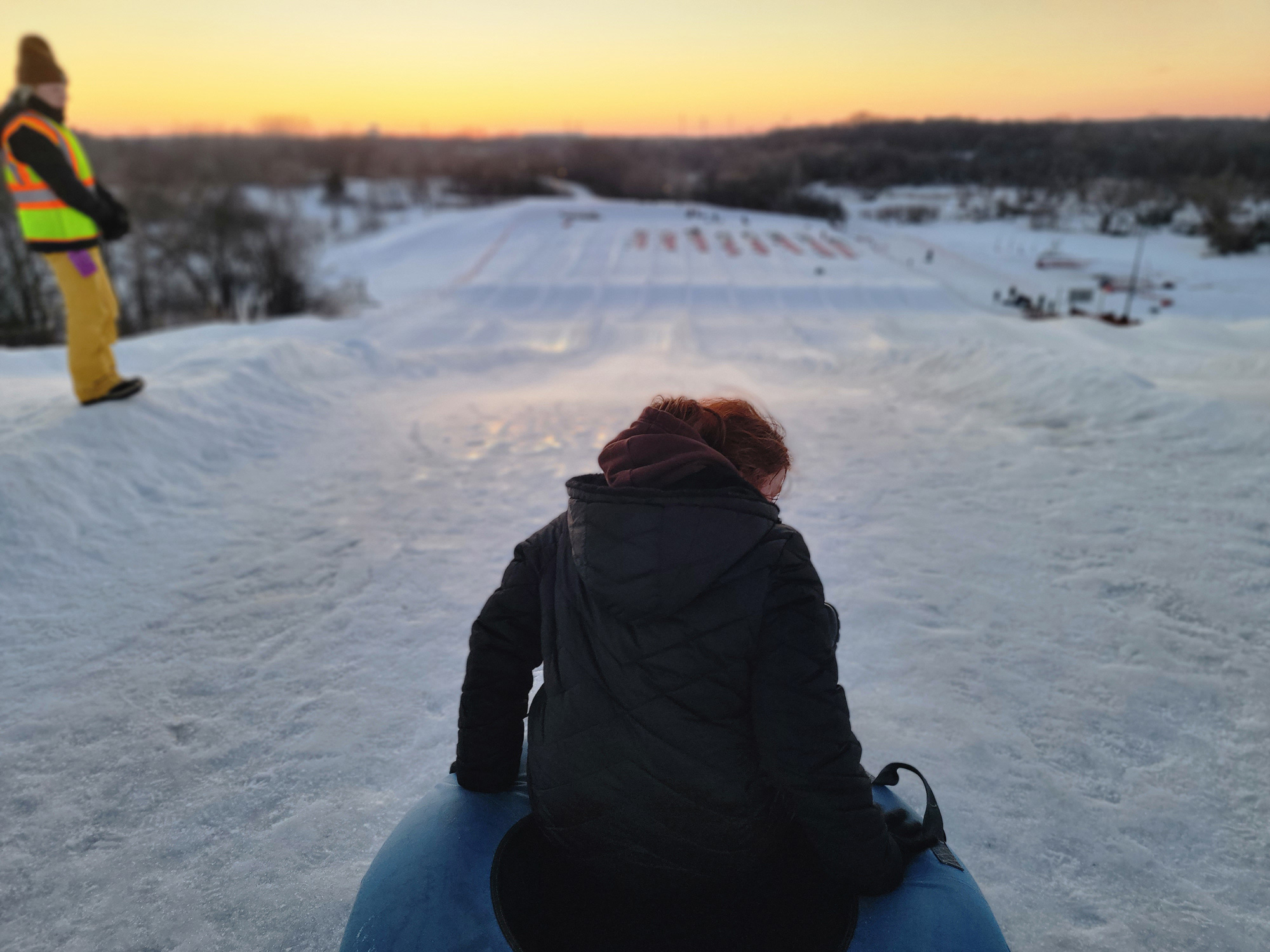 A young woman with red hair is on a slide going down a snowy hill on a sled