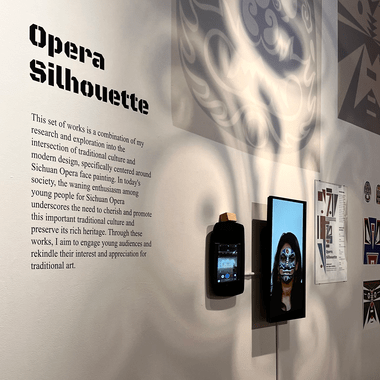 Image of Junlan's thesis exhibition work titled "Opera Silhouette." Includes vinyl didactic, tablet with interactive interface to take selfies with AR opera masks, and shadows from hanging prints of opera masks on transparent substrate.