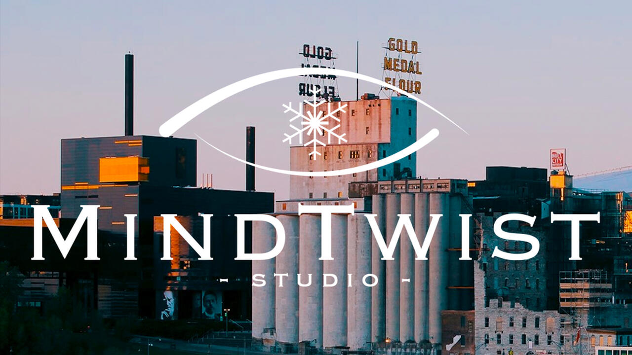 The logo of MindTwist studio, which is plain white text with a seemingly eye shape with a snowflake in the middle that is overlaid against a photograph of Minneapolis