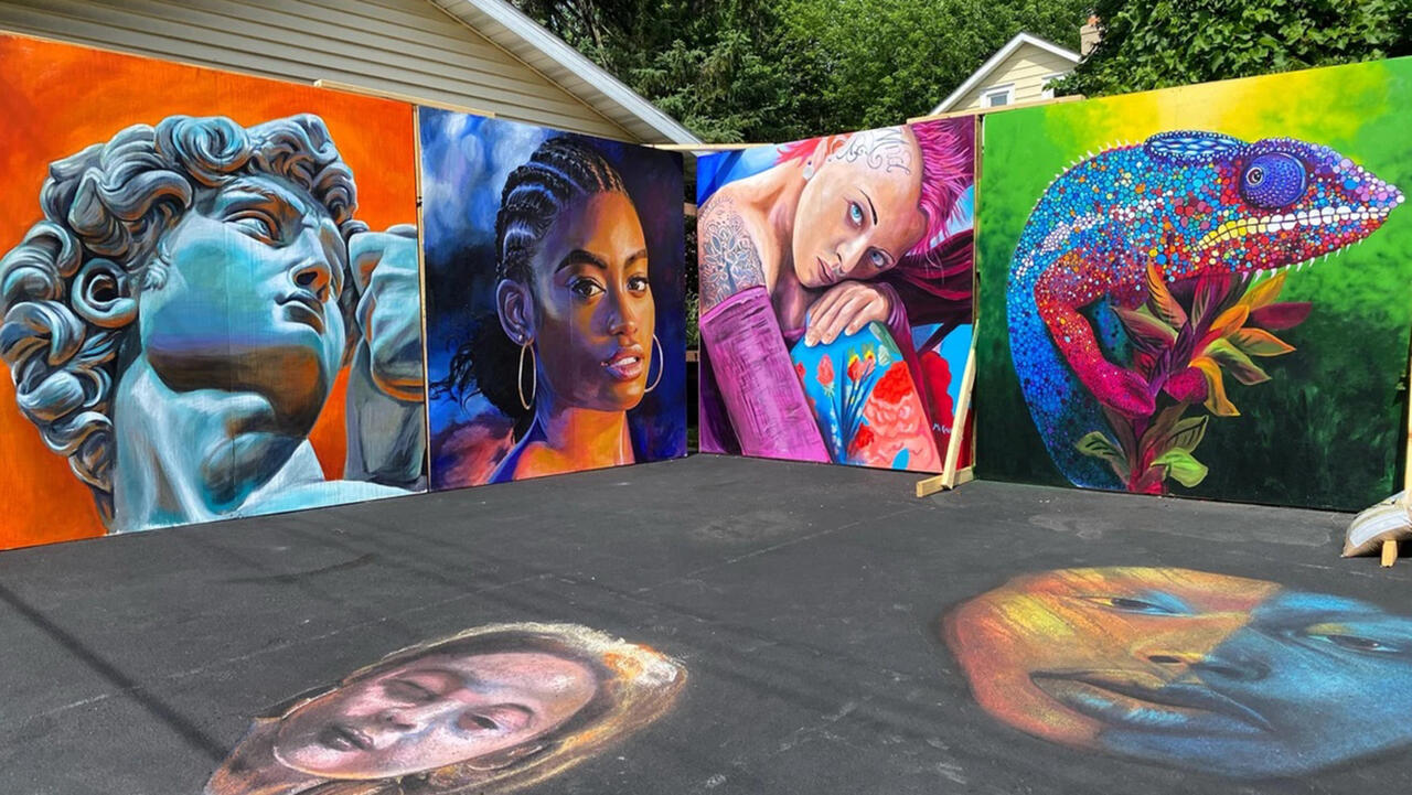Two large walls covered in different murals, one being a sculpture, one being of a woman with cornrows and large gold hoop earings, one of a woman with a bright pink mohawk and one of an iguana, all of these are incredibly colorful 