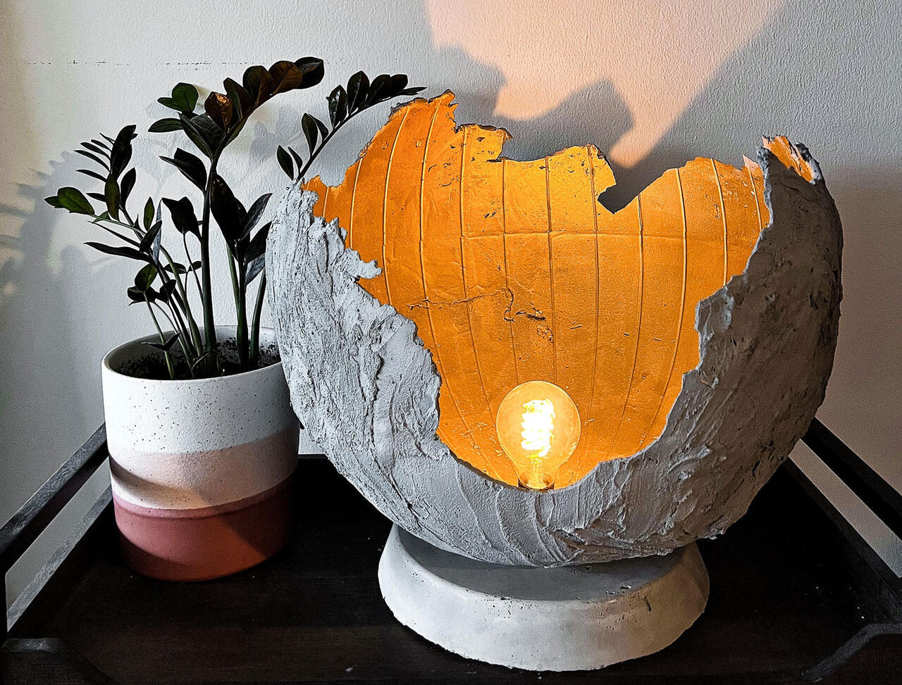 Handmade lamp next to a plant; the lamp appears to be made of paper mache