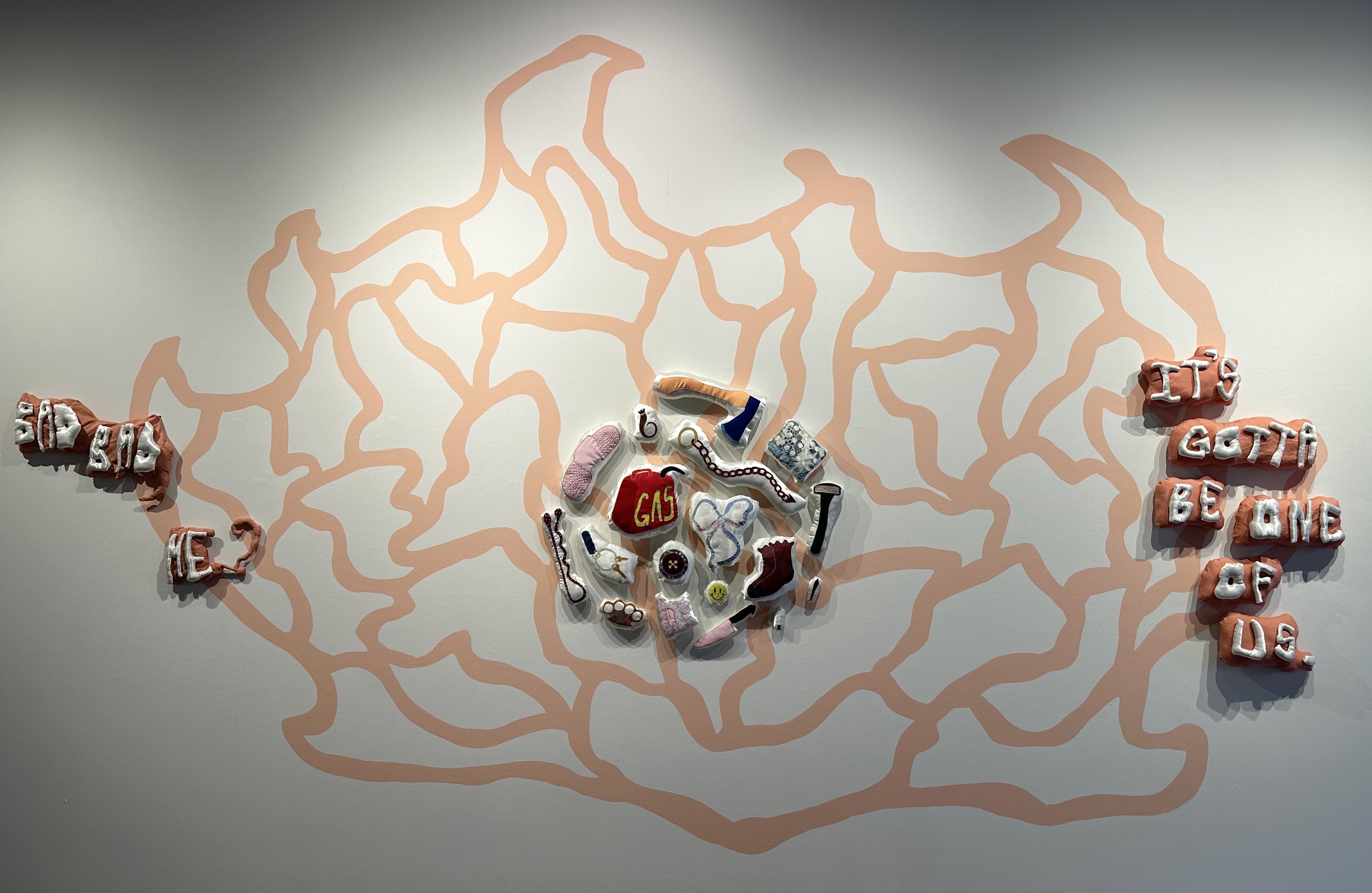 Artwork by Melanie Dowding: an orange-red, abstract painting on a white gallery wall. Several fabric sculptures are installed over the mural.