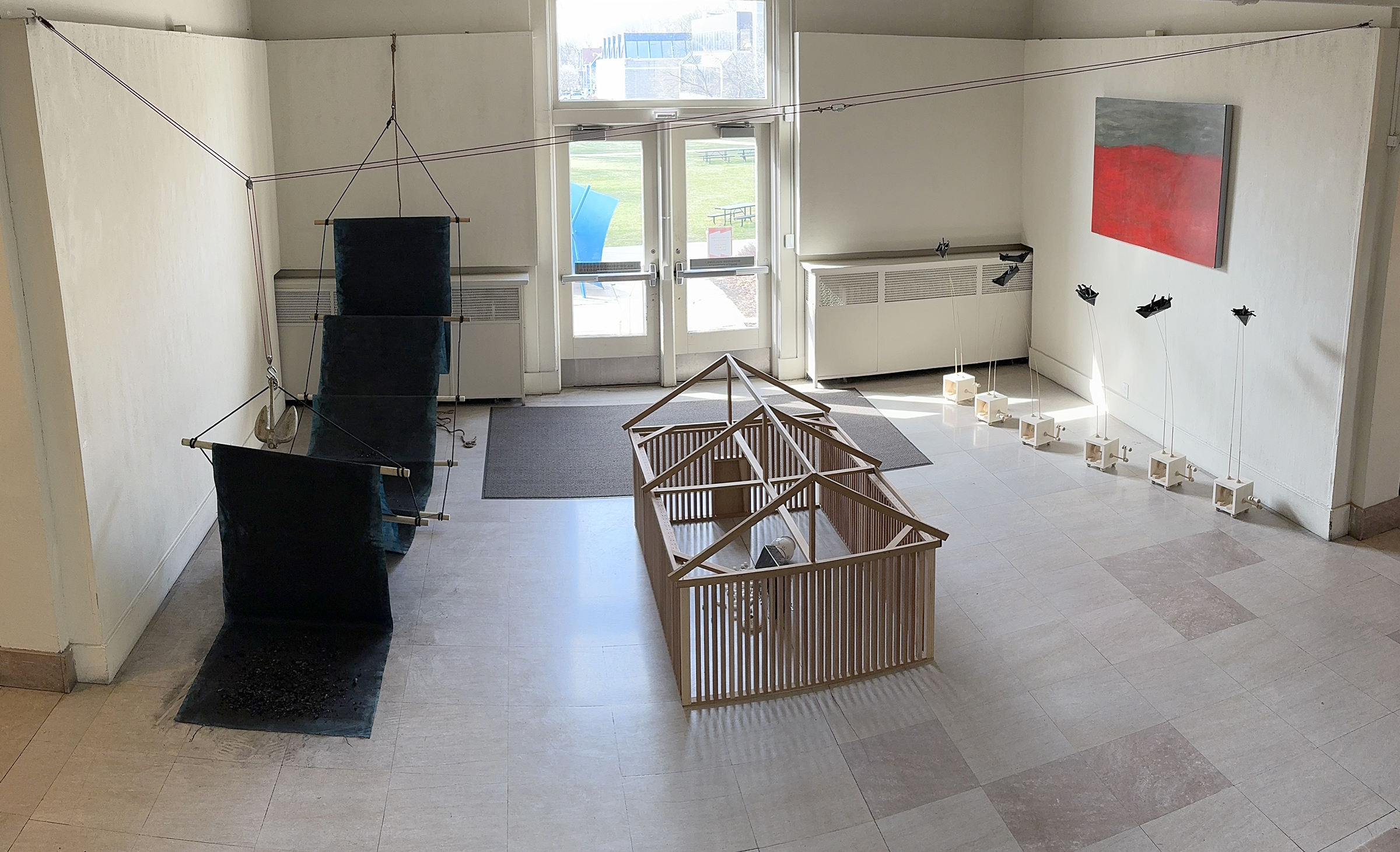 Image of Victor's thesis installation in the Morrison Building. Included are sculptures that are in part made of wood, paper, and charcoal. There is a grey and red painting on the far wall.