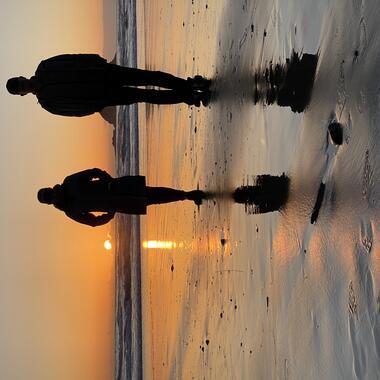 2 people standing side by side on a beach at sunset