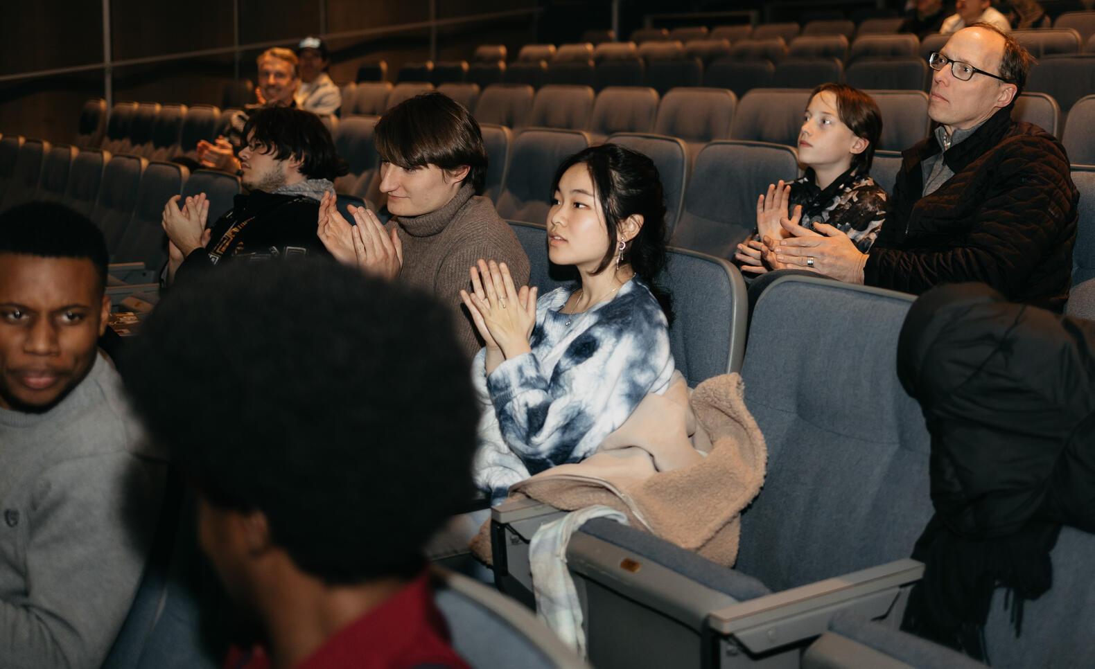 Pitch Event of Students Sitting in Auditorium 150 at MCAD. Students are clapping in a dark presentation environment 