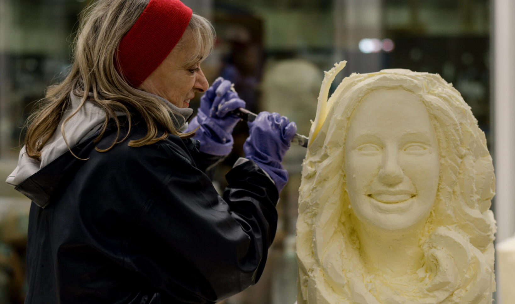 A woman is shown carving a bust of another woman out of butter
