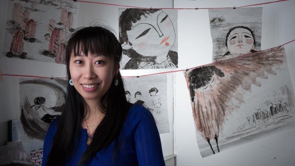 Wenwen sits in front of a collection of her paintings