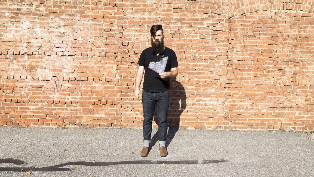 Portrait of Anthony Warnick, standing in front of a brick wall.