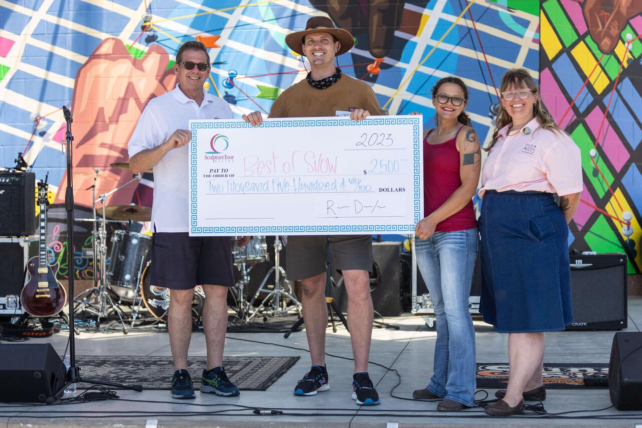 An image of four people, MCAD alum Cassi Rebman third from the left, holding up a check.