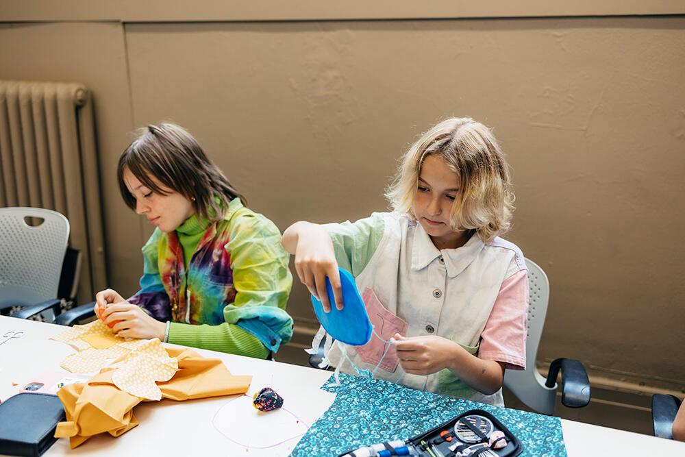 Two students sit at a table working with brightly colored felt. 