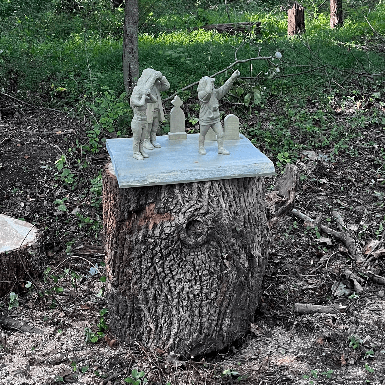 A picture of a sculpture consisting of three birdwatchers in a graveyard setting, resting on a tree stump.