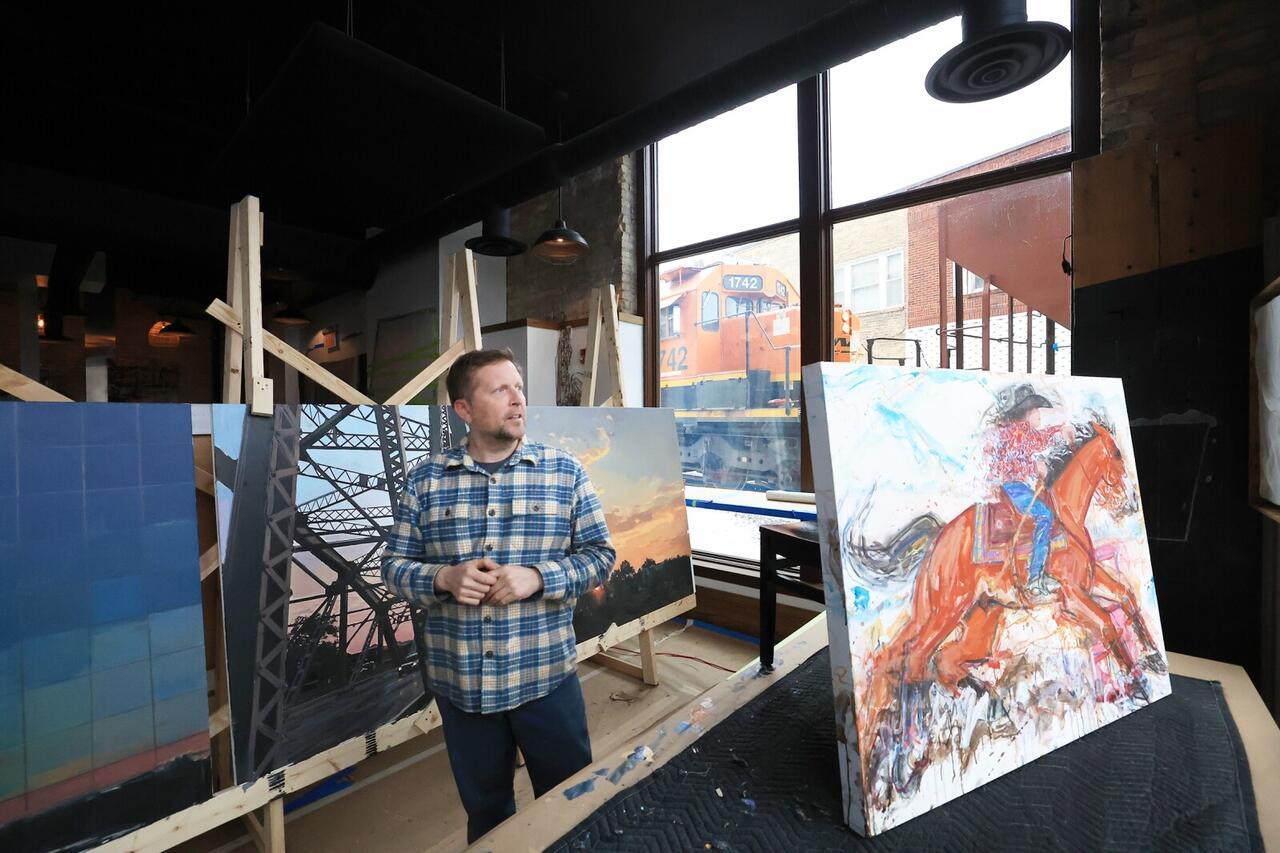 A photo of artist Casey Opstad working on his painting for a mural in a studio. 