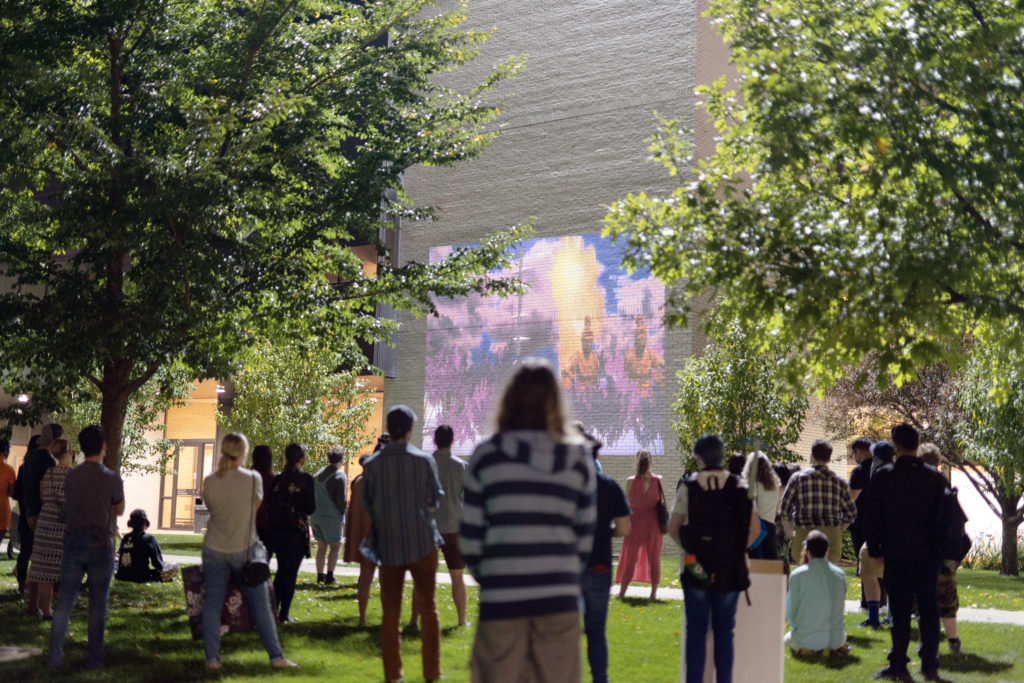 people watching a video projected on the outside of a building